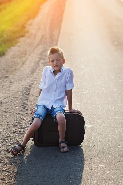 Das Kind sitzt an einem sonnigen Sommertag auf einem Koffer, die Reise — Stockfoto