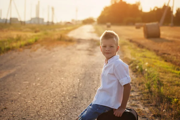 Das Kind sitzt an einem sonnigen Sommertag auf einem Koffer, die Reise — Stockfoto