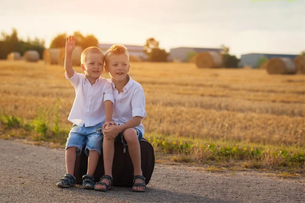 Due fratelli si siedono su una valigia sulla strada in estate al tramonto — Foto Stock