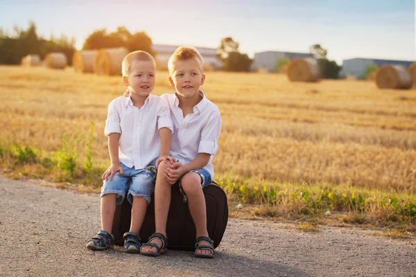 Twee broers zitten op een koffer op de weg in de zomer tijdens het zonnen — Stockfoto