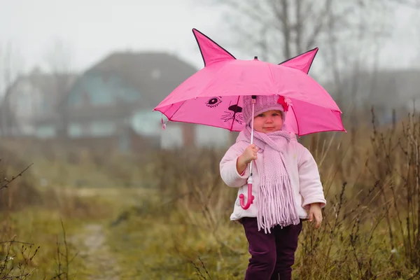 A menina bonito sob um guarda-chuva rosa no outono no outono — Fotografia de Stock