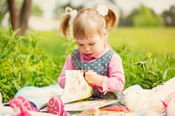 Маленькая девочка в весеннем парке читает книгу в теплый день — стоковое фото