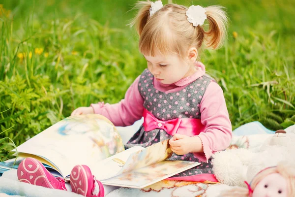 Маленькая милая девочка читает книгу в теплый солнечный день весной — стоковое фото