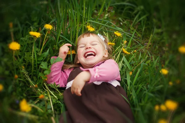 Bir çim ve gülüyor küçük mutlu kız yatıyor — Stok fotoğraf