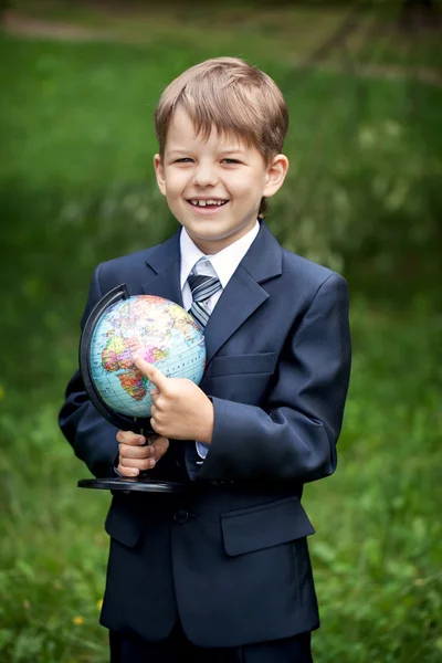 Cheerful schoolboy pointing at the globe in his hands outdoors — Stock Photo, Image