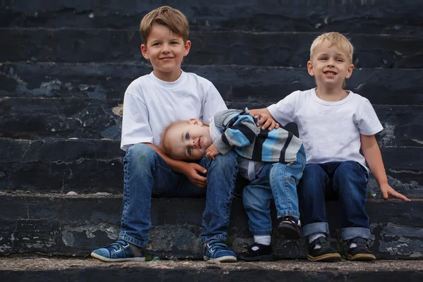 Little brother embracing with the brothers while sitting on a be — Stock Photo, Image