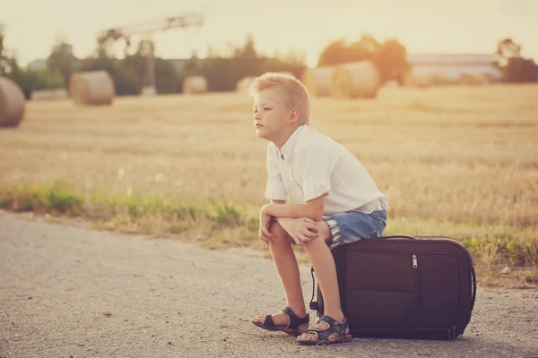 Das Kind sitzt an einem sonnigen Sommertag auf einem Koffer, die Reise — Stockfoto