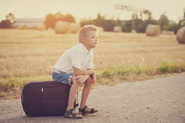 Il bambino si siede su una valigia nella giornata di sole estiva, il viaggio — Foto Stock