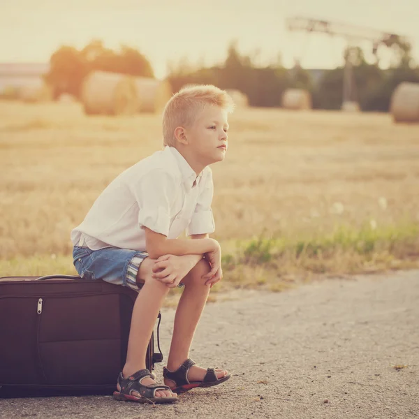 El niño se sienta en una maleta en el día soleado de verano, el viaje —  Fotos de Stock
