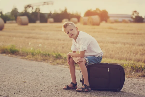El niño se sienta en una maleta en el día soleado de verano, el viaje — Foto de Stock