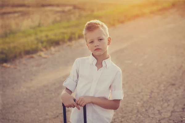 Ritratto di ragazzo tiene la maniglia di una valigia nella soleggiata da — Foto Stock