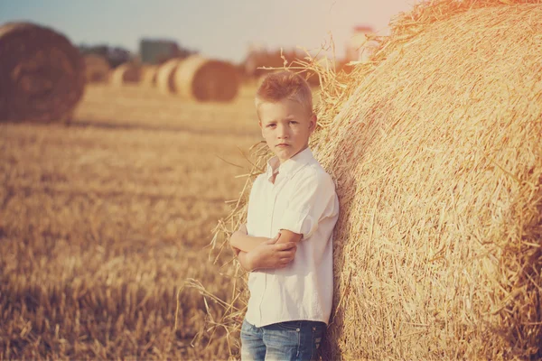 Der nette Junge auf dem Feld in der Nähe eines Strohstapels bei Sonnenuntergang — Stockfoto