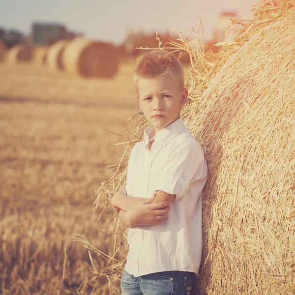 El niño agradable en el campo de cerca de pila de paja al atardecer —  Fotos de Stock