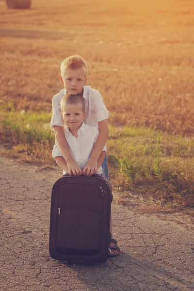 Deux frères avec une valise sur la route en été au coucher du soleil — Photo