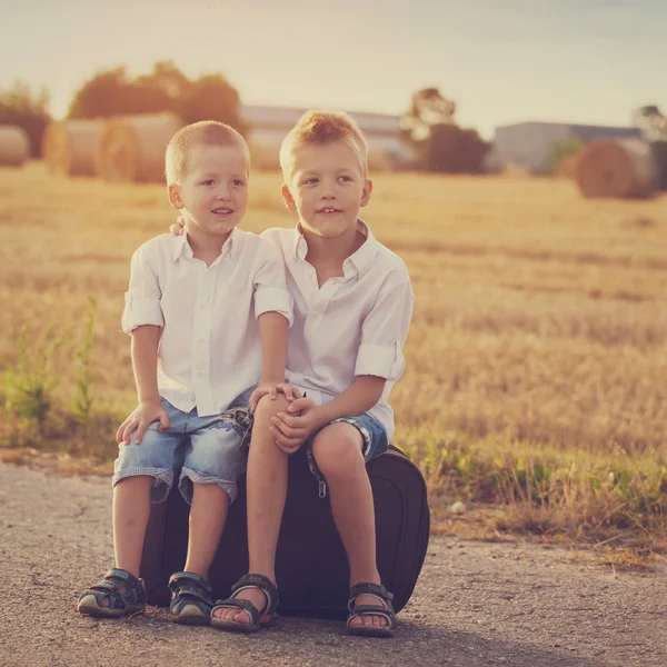 Due fratelli si siedono su una valigia sulla strada nell'estate a soli — Foto Stock