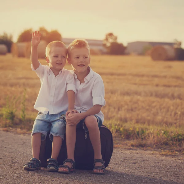 Dos hermanos se sientan en una maleta en la carretera en el verano al atardecer — Foto de Stock