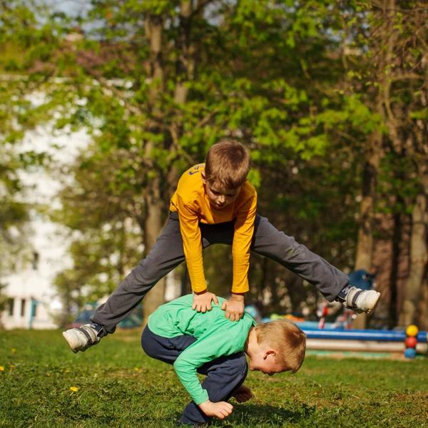 Due ragazzi allegri giocano all'aperto, saltano l'amico attraverso il fri — Foto Stock