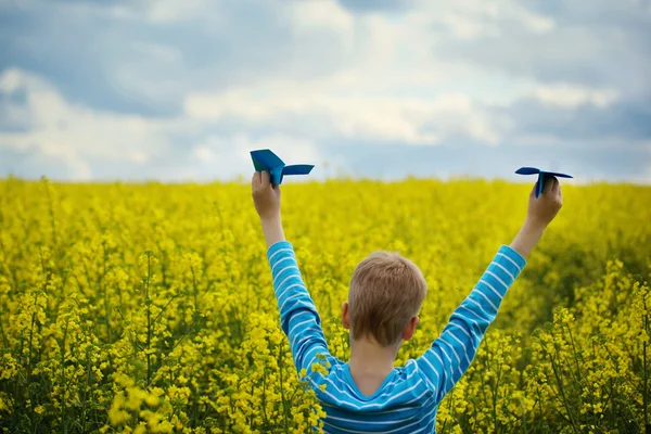 Menino com papel Avião contra céu azul e campo amarelo Flo — Fotografia de Stock