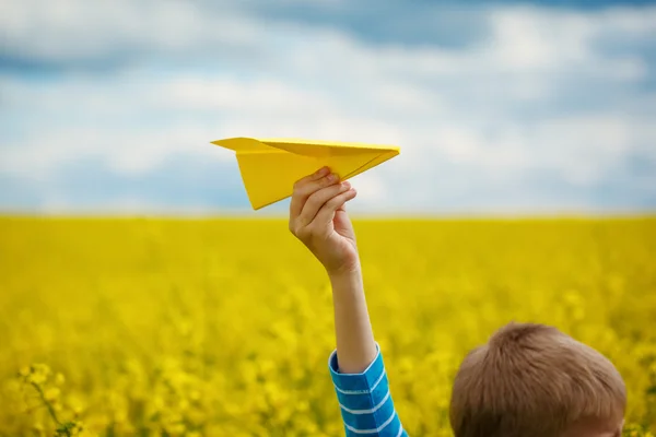 Avião de papel em crianças mãos sobre fundo amarelo e azul s — Fotografia de Stock