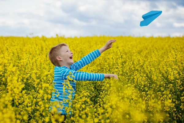 Happy boy leaning and throwing blue paper airplane on bright sun — Stock Photo, Image