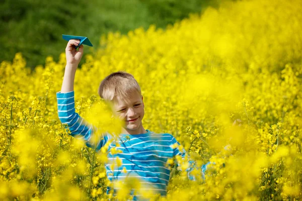 Felice ragazzo tiene in mano blu aeroplano di carta nella luminosa giornata di sole — Foto Stock