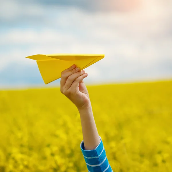 Papierflugzeug in Kinderhand auf gelbem Hintergrund und blauem s — Stockfoto