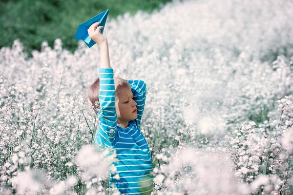 Happy boy holds in hand blue paper airplane on bright sunny day — Stock Photo, Image