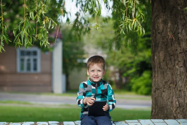 Pequeño chico sonrisa al aire libre usando su tableta —  Fotos de Stock