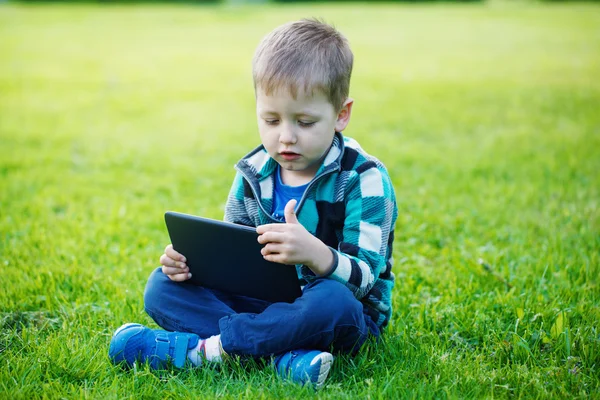 Liten pojke med tablett sitta på gräset — Stockfoto