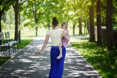 mother with the daughter on hands walk in park. rear view