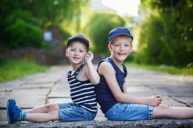 Two adorable little brothers sitting on stone on warm and sunny 