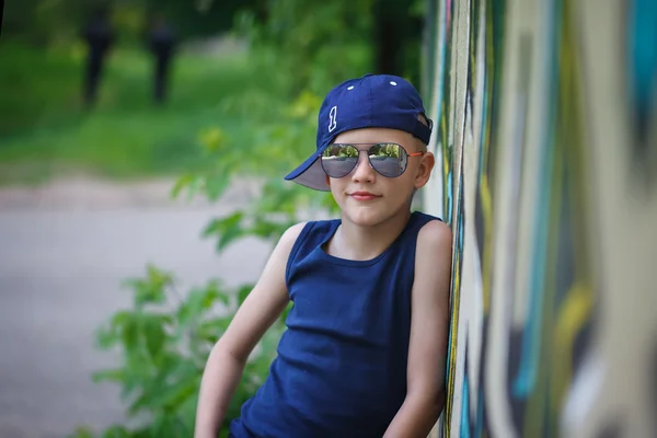 Ragazzino alla moda in occhiali da sole e cappello.Graffiti sfondo — Foto Stock