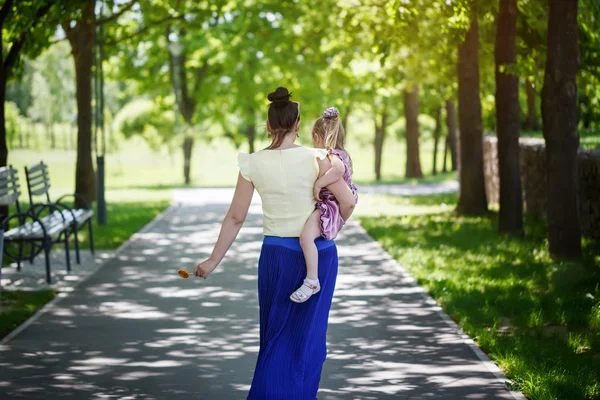 Mother with the daughter on hands walk in park. rear view — Zdjęcie stockowe