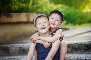 Two adorable little brothers laughing and hugging on warm and sunny  day 
