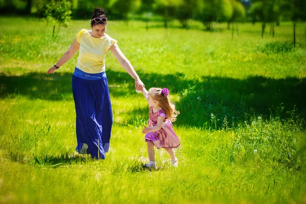 The little girl together with mother run and play on a grass in — Zdjęcie stockowe