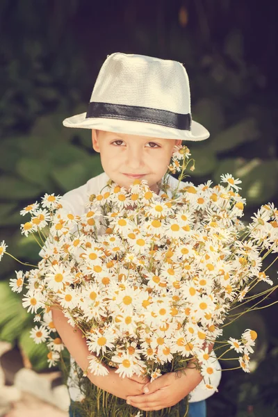 Ritratto adorabile ragazzo in un cappello con grande bouquet bianco di camomille. Ora legale. Tonificazione immagine — Foto Stock