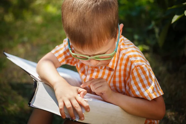 Söt baby pojke med glasögon läser boken i sommardag. Utomhus, tillbaka till skolan koncept. — Stockfoto