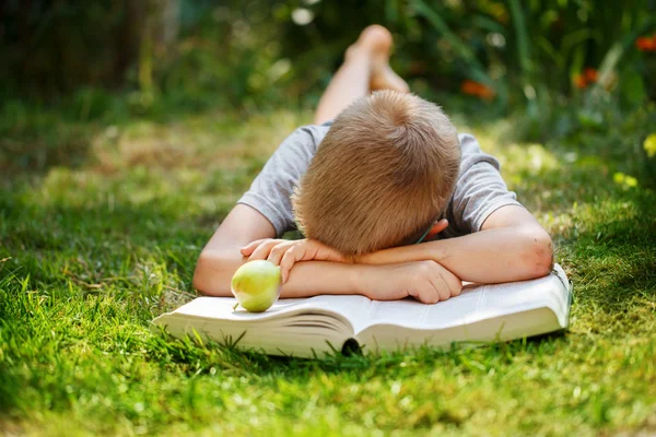 Милый школьник лежит на зеленой траве, который не хочет читать книгу. мальчик спит возле книг — стоковое фото