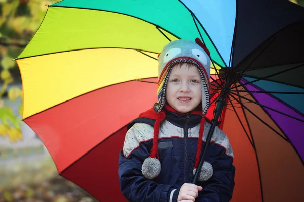 Piccolo ragazzo carino che cammina con grande ombrello all'aperto nel giorno di pioggia. Bambino divertendosi e indossando vestiti impermeabili colorati e cappuccio, concetto bambini . — Foto Stock