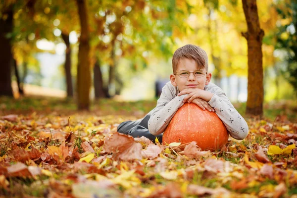 Aranyos kisfiú támaszkodva egy tök, őszi idő. — Stock Fotó