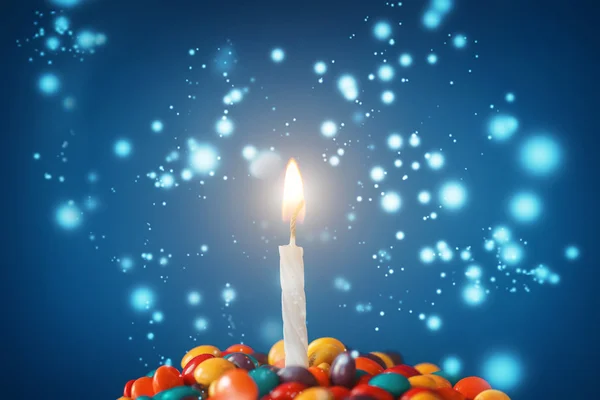 Świeczki urodzinowe na pyszne ciastko z cukierków i blask na światło niebieskie tło. Kartkę z życzeniami wakacje — Zdjęcie stockowe