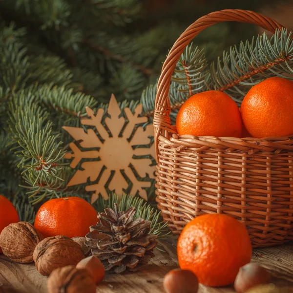 Basket with tangerines, cones, nuts and fir branches on wooden b — Stock Photo, Image