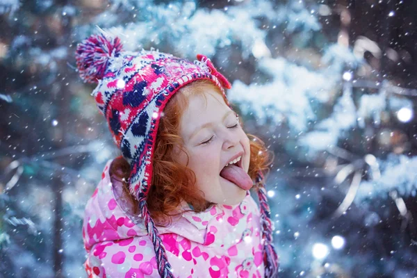 Portrait of a cute little girl who catches snowflakes mouth in w