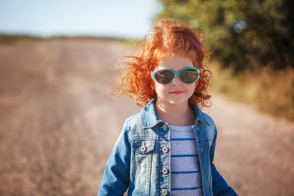 Портрет Милая маленькая красная кудряшка в солнечных очках в солнечный день — стоковое фото