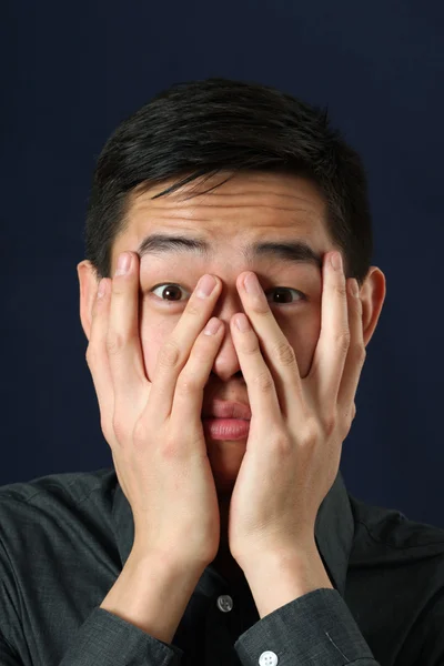Asiático homem olhando através de seus dedos — Fotografia de Stock