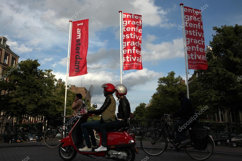 AMSTERDAM, NETHERLANDS - AUGUST 9, 2012: Two people drive on a Vespa scooter over the bridge decorated with banners with an official brand of the city in Amsterdam, Netherlands.