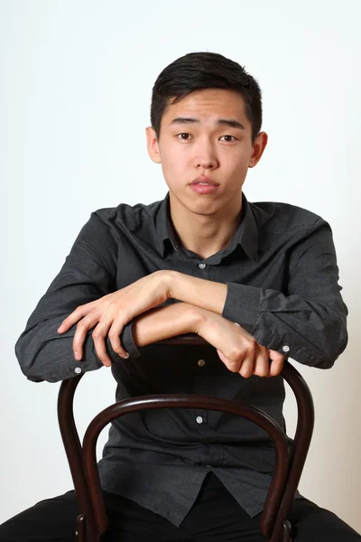 Fiatal ázsiai ember ül egy széken — Stock Fotó