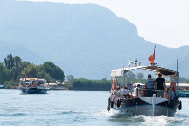Nehirde yüzen turistli tekneler dağların arka planında