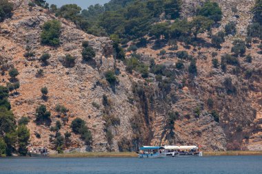 Bir turist teknesi dağların önünde duruyor.