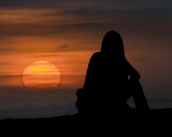 Женщина, сидящая и наблюдающая за закатом — стоковое фото
